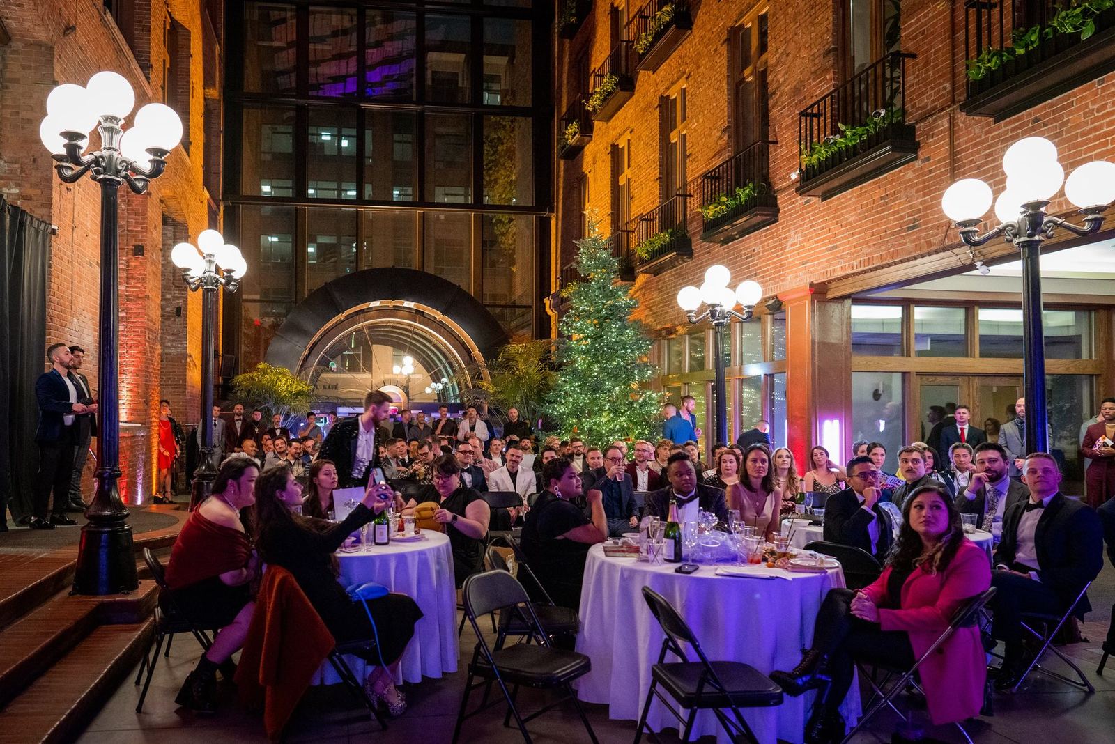 Guests at dinner tables in a lantern-lit brick courtyard at a wayOUT Seattle event